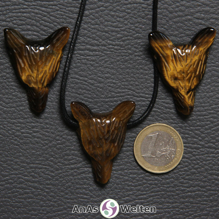 Drei Tigerauge Wolf Anhänger nebeneinander. Einer befindet sich an einem schwarzen Baumwollband.