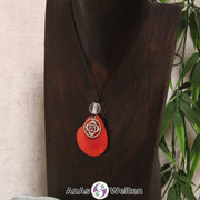 Eine rote Tagua-Nuss Chakra Kette mit silberfarbenem 1. Chakra Symbol und Bergkristallkugel an einer dunklen Büste.