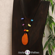 Eine orangene Tagua-Nuss Scheibe als Chakra Kette mit 6 Tagua-Splittern in den anderen Chakrafarben an einer dunklen Büste.