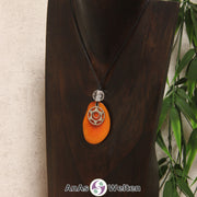 Eine orangene Tagua-Nuss Chakra Kette mit silberfarbenem 2. Chakra Symbol und Bergkristallkugel an einer dunklen Büste.