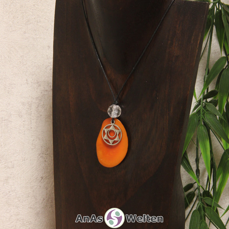 Eine orangene Tagua-Nuss Chakra Kette mit silberfarbenem 2. Chakra Symbol und Bergkristallkugel an einer dunklen Büste.
