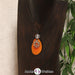 Eine orangene Tagua-Nuss Chakra Kette mit silberfarbenem 2. Chakra Symbol und Bergkristallkugel an einer dunklen Büste.