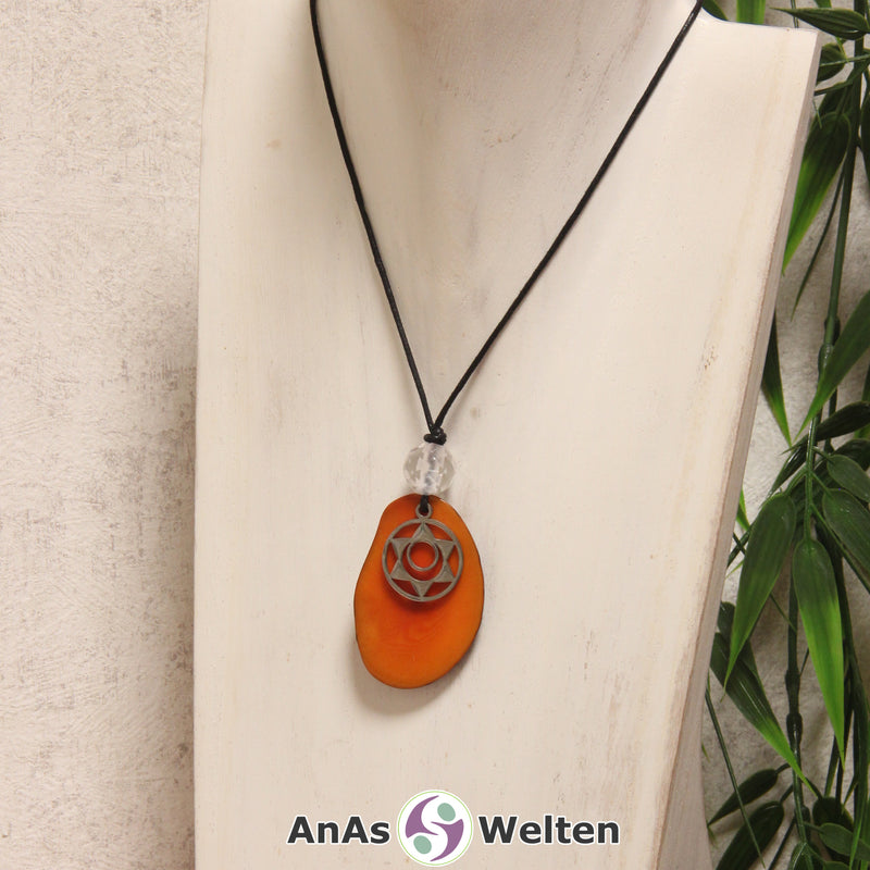 Das Produktbild für die 2. Chakra (Sakralchakra) Symbol Kette orange zeigt eine orange gefärbte Tagua-Nuss-Scheibe an einem schwarzen Baumwollband, vor der ein silberfarbener Anhänger mit dem Chakrasymbol befestigt ist. Die Nuss-Scheibe hat einen dunklen Rand und eine glänzende Oberfläche. Direkt darüber befindet sich eine Bergkristallkugel.