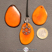 Drei orange gefärbte Tagua-Nuss-Scheiben. Eine davon ist als Kette mit Bergkristall und 2. Chakra Symbol gebunden.
