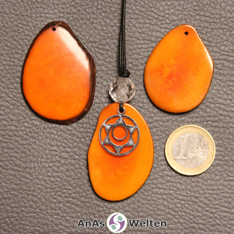 Drei orange gefärbte Tagua-Nuss-Scheiben. Eine davon ist als Kette mit Bergkristall und 2. Chakra Symbol gebunden.