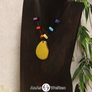 Eine gelbe Tagua-Nuss Scheibe als Chakra Kette mit 6 Tagua-Splittern in den anderen Chakrafarben an einer dunklen Büste.