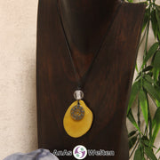 Eine gelb Tagua-Nuss Chakra Kette mit silberfarbenem 3. Chakra Symbol und Bergkristallkugel an einer dunklen Büste.