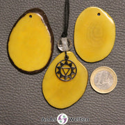 Drei gelb gefärbte Tagua-Nuss-Scheiben. Eine davon ist als Kette mit Bergkristall und 3. Chakra Symbol gebunden.