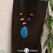 Eine türkise Tagua-Nuss Scheibe als Chakra Kette mit 6 Tagua-Splittern in den anderen Chakrafarben an einer dunklen Büste.