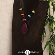 Eine lila Tagua-Nuss Scheibe als Chakra Kette mit 6 Tagua-Splittern in den anderen Chakrafarben an einer dunklen Büste.