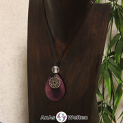 Eine lila Tagua-Nuss Chakra Kette mit silberfarbenem 7. Chakra Symbol und Bergkristallkugel an einer dunklen Büste.