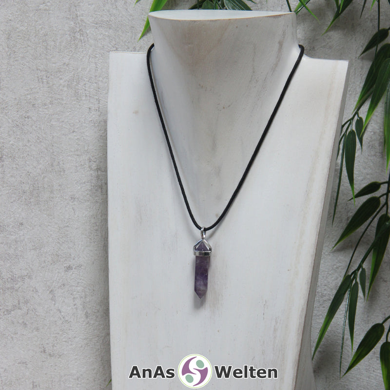 Das Produktbild zeigt einen Amethyst Stift-Anhänger groß an einem Baumwollband. Es handelt sich um einen Stift-Anhänger mit Doppelspitze in einer lila-weißen Farbe. Direkt unterhalb der oberen Spitze ist ein glänzendes Metallelement befestigt, das oberen Ende einen Bogen mit einer Öse hat.