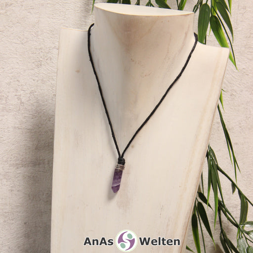 Amethyst Stift-Anhänger klein mit Kette: Das Bild zeigt einen Amethyst Stift-Anhänger klein mit Kette. Der Stift-Anhänger ist lila mit einem weißen Einschluss. Am oberen Ende verbindet ein silberfarbenes Element den Edelstein mit der Stoffkordel.