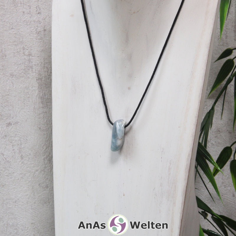 Ein blauer Aquamarin gebohrter Trommelstein an einem schwarzen Baumwollband, der um eine helle Büste gehängt wurde.