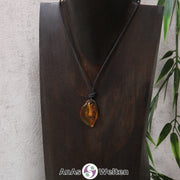 Ein gold-brauner Bernstein gebohrter Trommelstein an einem schwarzen Baumwollband, der um eine dunkle Büste gehängt wurde.