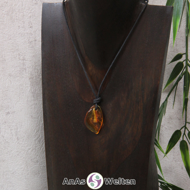 Ein gold-brauner Bernstein gebohrter Trommelstein an einem schwarzen Baumwollband, der um eine dunkle Büste gehängt wurde.