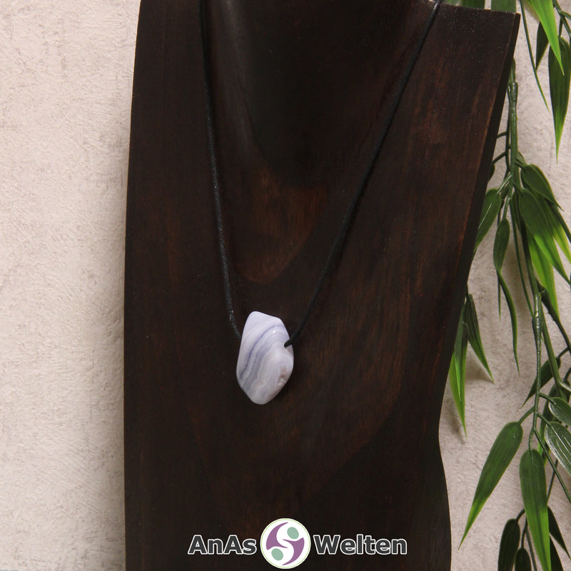 Ein gebohrter blauer Chalcedon Trommelstein an einem Baumwollband. In dem Edelstein kann man gut die verschiedenen Schichten aus unterschiedlichen Blautönen sehen, wodurch er gestreift aussieht.