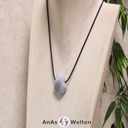 Ein blauer Chalcedon gebohrter Trommelstein an einem schwarzen Baumwollband, der um eine helle Büste gehängt wurde.