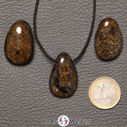 Drei braune Bronzit gebohrte Trommelsteine nebeneinander. Einer befindet sich an einem schwarzen gewachsten Baumwollband.