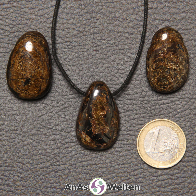 Drei braune Bronzit gebohrte Trommelsteine nebeneinander. Einer befindet sich an einem schwarzen gewachsten Baumwollband.