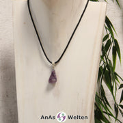 Ein lila Charoit Stein mit Öse an einem schwarzen Baumwollband, der um eine helle Büste gehängt wurde.