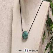 Ein blau-grüner Chrysokoll gebohrter Trommelstein an einem schwarzen Baumwollband, der um eine helle Büste gehängt wurde.