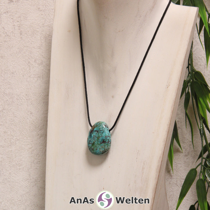 Ein blau-grüner Chrysokoll gebohrter Trommelstein an einem schwarzen Baumwollband, der um eine helle Büste gehängt wurde.