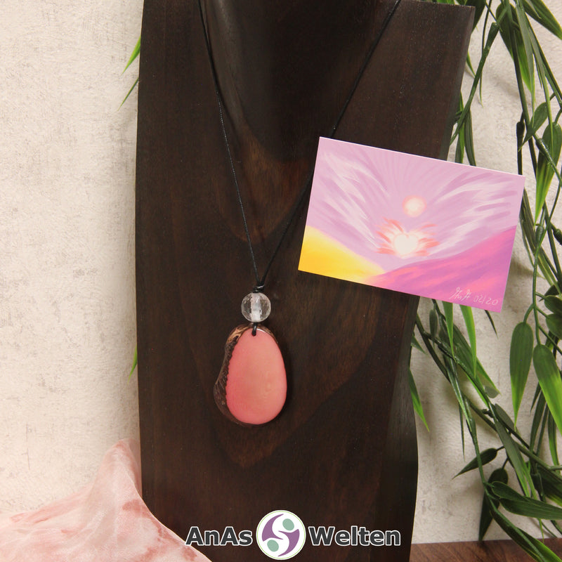 Ein rosa Tagua-Nuss Engel Anhänger ist als Kette mit einer Bergkristallkugel um eine dunkle Büste gehängt.