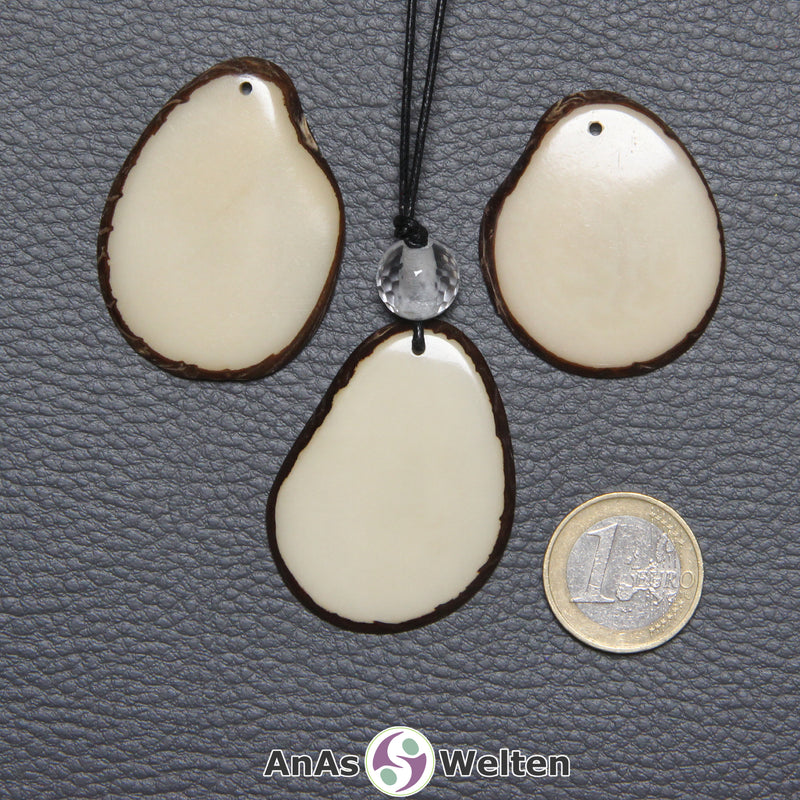 Drei Tagua-Nuss-Scheiben in Naturfarbe. Die mittlere ist mit einer Bergkristallkugel an ein schwarzes Baumwollband gebunden.