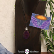 Ein lila Tagua-Nuss Engel Anhänger ist als Kette mit einer Bergkristallkugel um eine dunkle Büste gehängt.