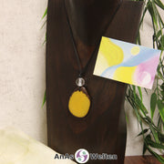 Das Produktbild für die Engel Kette Erzengel Jophiel mit Karte zeigt eine in einem Gelb gefärbte Tagua-Nuss-Scheibe an einem schwarzen Baumwollband. Die Nuss-Scheibe hat einen dunklen Rand und eine glänzende Oberfläche. Direkt darüber befindet sich eine facettierte Bergkristallkugel. Rechts neben der Kette sieht man außerdem die Erzengel Jophiel Karte, die den Engel als abstraktes Bild zeigt.