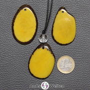 Drei Tagua-Nuss-Scheiben in Gelb. Die mittlere ist mit einer Bergkristallkugel an ein schwarzes Baumwollband gebunden.