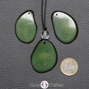 Drei Tagua-Nuss-Scheiben in Grün. Die mittlere ist mit einer Bergkristallkugel an ein schwarzes Baumwollband gebunden.