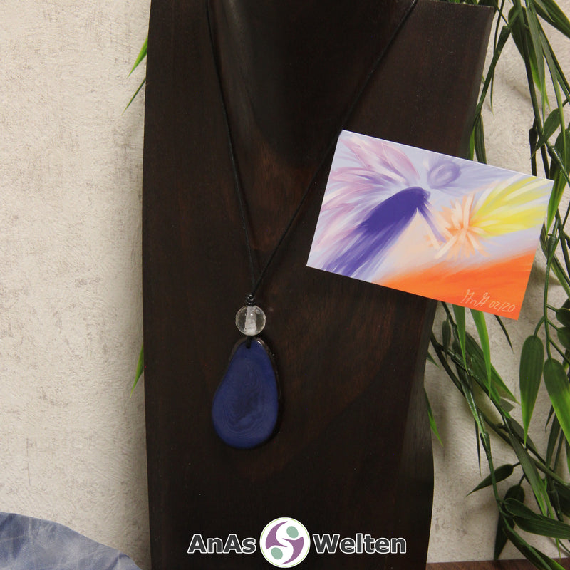 Ein blauer Tagua-Nuss Engel Anhänger ist als Kette mit einer Bergkristallkugel um eine dunkle Büste gehängt.