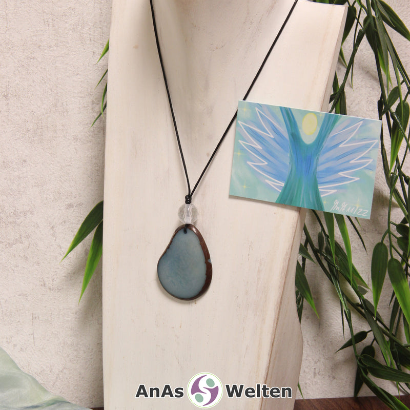 Ein blauer Tagua-Nuss Engel Anhänger ist als Kette mit einer Bergkristallkugel um eine dunkle Büste gehängt.