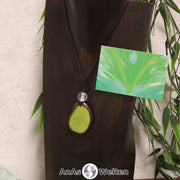 Ein grüner Tagua-Nuss Engel Anhänger ist als Kette mit einer Bergkristallkugel um eine dunkle Büste gehängt.