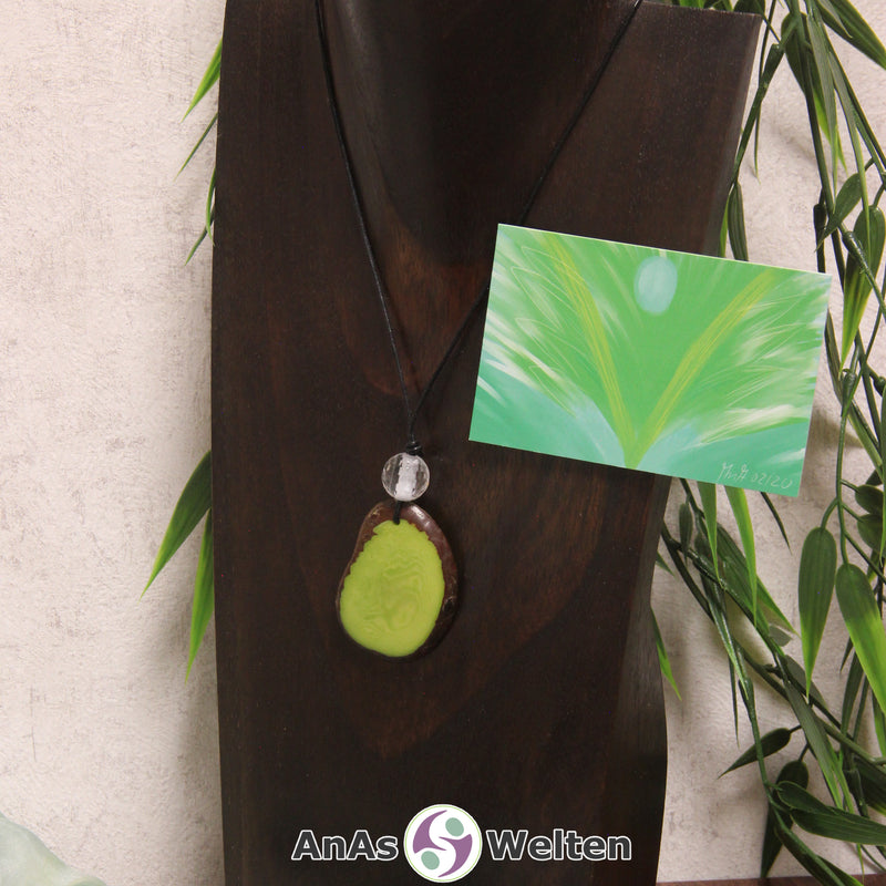 Ein grüner Tagua-Nuss Engel Anhänger ist als Kette mit einer Bergkristallkugel um eine dunkle Büste gehängt.