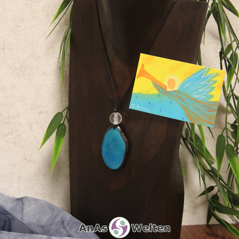 Ein türkiser Tagua-Nuss Engel Anhänger ist als Kette mit einer Bergkristallkugel um eine dunkle Büste gehängt.