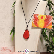 Das Produktbild für die Engel Kette Erzengel Uriel mit Karte zeigt eine in einem kräftigen Rot gefärbte Tagua-Nuss-Scheibe an einem schwarzen Baumwollband. Die Nuss-Scheibe hat einen dunklen Rand und eine glänzende Oberfläche. Direkt darüber befindet sich eine facettierte Bergkristallkugel. Rechts neben der Kette sieht man außerdem die Erzengel Uriel Karte, die den Engel als abstraktes Bild zeigt.