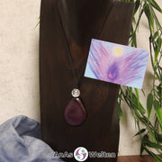 Ein lilafarbener Tagua-Nuss Engel Anhänger ist als Kette mit einer Bergkristallkugel um eine dunkle Büste gehängt.