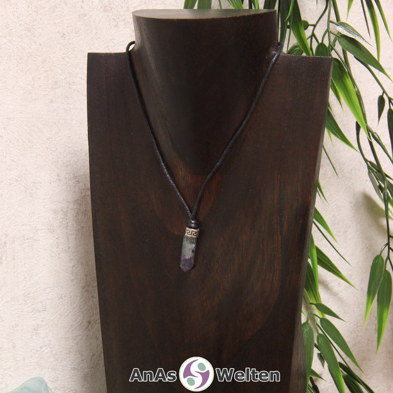 Eine grün-lila Fluorit Stift-Anhänger klein Kette mit einem Metallelement über dem Edelstein an einer dunklen Büste.