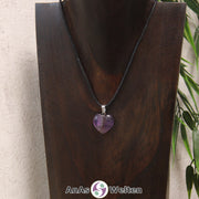 Ein Amethyst Herz Anhänger an einem schwarzen Baumwollband, der um eine dunkle Büste gehängt wurde.