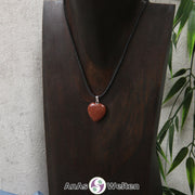 Das Bild zeigt einen Herzanhänger Goldfluss-Herz an einem schwarzen Baumwollband. Der Edelstein wurde in eine Herzform geschliffen und verfügt über eine silberfarbene Öse an der Oberseite. Er hat eine rotbraune Farbe, die von einem goldenen Glitzern durchzogen ist.