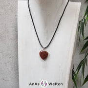 Ein Goldfluss Herz Anhänger an einem schwarzen Baumwollband, der um eine helle Büste gehängt wurde.