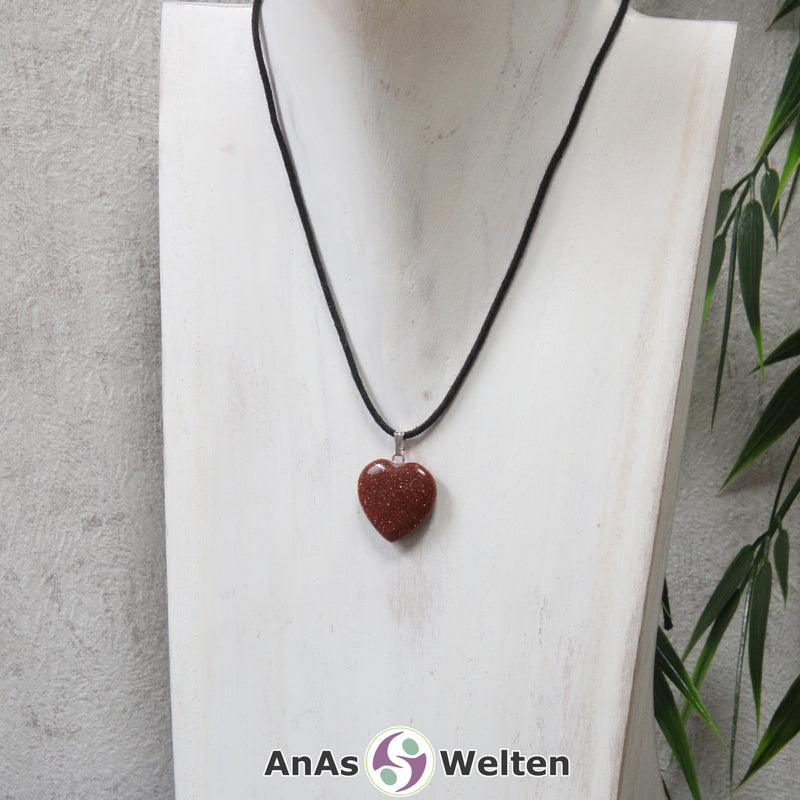 Ein Goldfluss Herz Anhänger an einem schwarzen Baumwollband, der um eine helle Büste gehängt wurde.