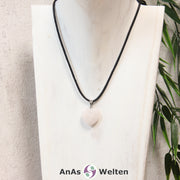 Ein Rosenquarz Herz Anhänger an einem schwarzen Baumwollband, der um eine helle Büste gehängt wurde.