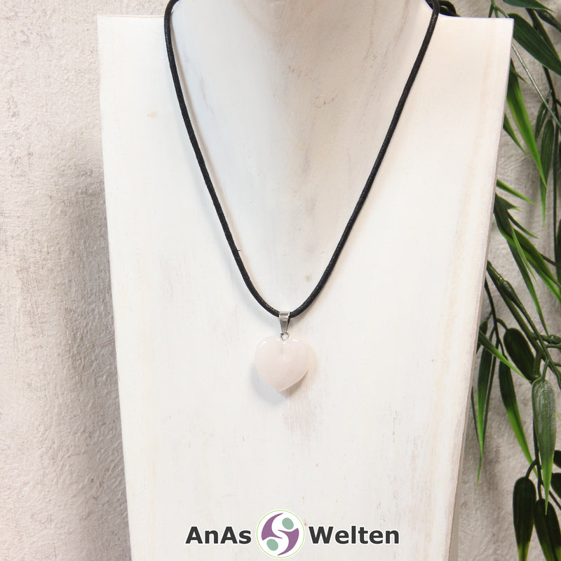 Ein Rosenquarz Herz Anhänger an einem schwarzen Baumwollband, der um eine helle Büste gehängt wurde.