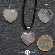 Drei Herzanhänger aus Rosenquarz nebeneinander. Einer befindet sich an einem schwarzen gewachsten Baumwollband.