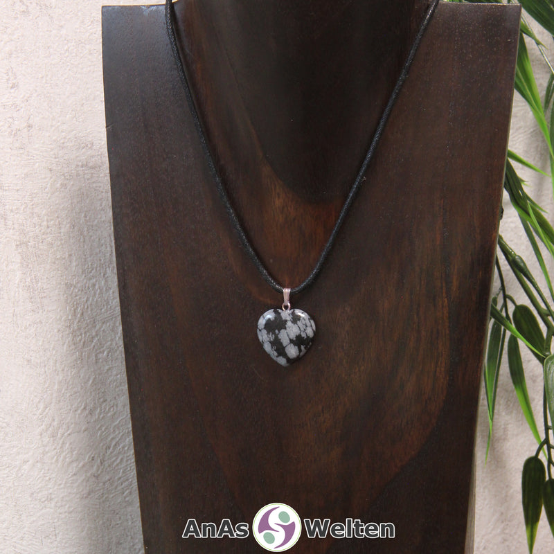 Ein Schneeflocken-Obsidian Herz Anhänger an einem schwarzen Baumwollband, der um eine dunkle Büste gehängt wurde.