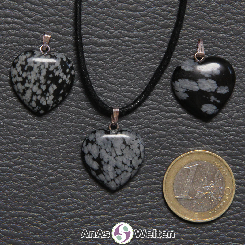 Drei Herzanhänger aus Schneeflocken-Obsidian nebeneinander. Einer befindet sich an einem schwarzen gewachsten Baumwollband.